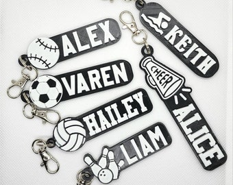 May include: Six black and white personalized keychains with different sports-themed icons. The keychains feature the names "Alex", "Varen", "Hailey", "Liam", "Alice", and "Keith".