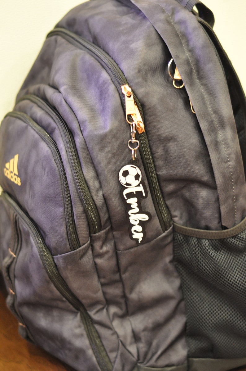 May include: A dark blue backpack with a zipper pull featuring a soccer ball and the name "Timber".