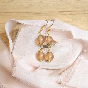 May include: A pair of gold dangle earrings with three translucent brown glass beads on each earring.