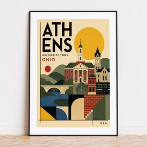 May include: A framed travel poster featuring a stylized illustration of Athens, Ohio. The text reads ATHENS UNIVERSITY TOWN OHIO and USA. The design includes a red brick building with a white steeple, a clock tower, a bridge, and a yellow sun.