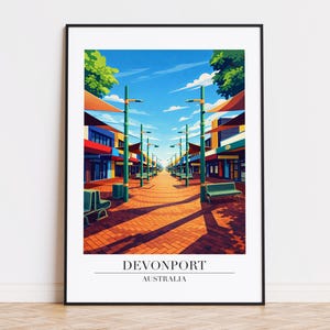 May include: A framed art print of Devonport, Australia, showing a colourful street scene. The artwork depicts a pedestrian walkway with shops, green benches, and streetlights under a bright blue sky, with the text "Devonport Australia".