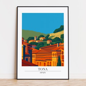 May include: A framed art print featuring a stylized illustration of Tona, Spain. The artwork depicts a village with orange rooftops, green hills, and a blue sky. The text "TONA" and "SPAIN" are printed at the bottom.
