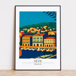 May include: A framed art print showing a colourful illustration of Sète, France. The image features buildings along a waterfront, with boats and a green hill in the background. The text "Sète France" is at the bottom of the print.