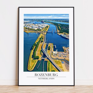 May include: A framed print featuring an aerial view of Rozenburg, Netherlands. The image showcases a waterway with bridges, roads, and industrial structures. The print has a black frame and the text "ROZENBURG NETHERLANDS" at the bottom.