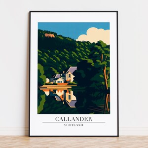 Op de afbeelding: Een ingelijste kunstdruk met een gestileerd landschap van Callander, Schotland. Het kunstwerk toont een wit huis met een donker dak dat weerspiegeld wordt in het water, omringd door groene bomen en een blauwe lucht. De tekst "CALLANDER SCOTLAND" staat onderaan.