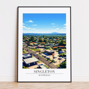 Puede incluir: Una impresión enmarcada que muestra una vista aérea de Singleton, Australia, bajo un cielo azul brillante con nubes dispersas. La imagen muestra una ciudad con casas, carreteras y edificios comerciales. El texto "SINGLETON AUSTRALIA" se muestra en la parte inferior.