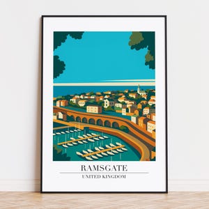 Puede incluir: Una impresión artística enmarcada que presenta una ilustración estilizada de Ramsgate, Reino Unido. La obra de arte representa una ciudad costera con un puente, un puerto y barcos, bajo un cielo azul. La impresión incluye el texto "RAMSGATE UNITED KINGDOM".