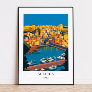 May include: A framed art print of Sciacca, Italy, featuring a stylized illustration of a coastal town. The artwork depicts colorful buildings, boats in the harbor, and a clear blue sky. The text "SCIACCA ITALY" is at the bottom.