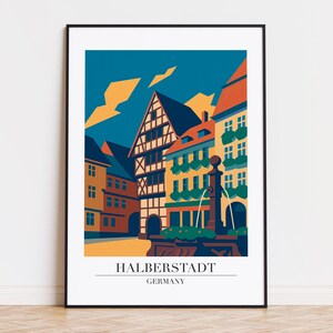 Puede incluir: Una impresión artística enmarcada con una ilustración estilizada de Halberstadt, Alemania. La obra representa edificios coloridos, una fuente y un cielo azul con acentos naranjas. El texto "HALBERSTADT GERMANY" está en la parte inferior.