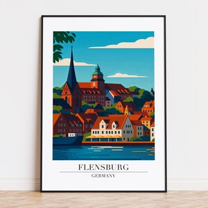 Puede incluir: Una impresión artística enmarcada que presenta una ilustración estilizada de Flensburgo, Alemania. La obra de arte representa un paisaje urbano con edificios de tejados rojos, una alta aguja de iglesia y una masa de agua, sobre un cielo azul. El texto "FLENSBURG GERMANY" está en la parte inferior.