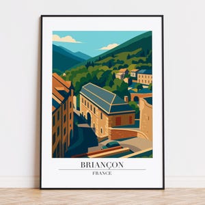 May include: A framed art print featuring a stylized illustration of Briançon, France. The artwork depicts buildings, a bridge, and mountains in shades of tan, green, and blue. The text "BRIANÇON FRANCE" is at the bottom.