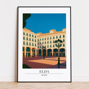 Puede incluir: Una impresión artística enmarcada que presenta una ilustración estilizada de Elda, España. La obra de arte representa una plaza con arcos, edificios y farolas bajo un cielo azul. El texto "ELDA" y "SPAIN" se encuentran en la parte inferior.