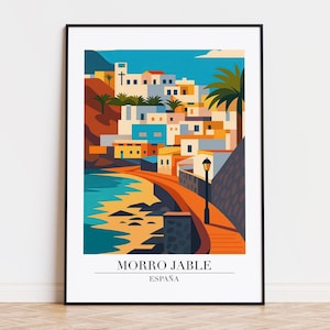 May include: A framed art print featuring a colorful illustration of Morro Jable, Spain. The artwork depicts a coastal town with white buildings, palm trees, and a pathway along the shore. The text "MORRO JABLE ESPAÑA" is at the bottom.