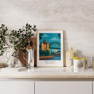 Może przedstawiać: Oprawiony wydruk artystyczny przedstawiający stylizowaną ilustrację Newcastle, Wielka Brytania. Grafika przedstawia zamek, most i tekst "Newcastle United Kingdom" w złotej ramie. Paleta kolor&oacute;w obejmuje odcienie niebieskiego, zielonego i ż&oacute;łtego.
