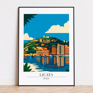 May include: A framed art print featuring a stylized illustration of Licata, Italy. The artwork depicts a coastal town with buildings in shades of orange and brown, set against a blue sky and sea. The word "LICATA" and "ITALY" are printed at the bottom.