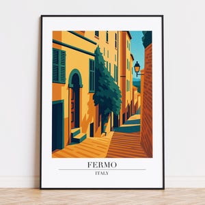 Puede incluir: Una impresión artística enmarcada que presenta una ilustración estilizada de una escena callejera en Fermo, Italia. La obra de arte representa edificios en tonos amarillos y naranjas, con un cielo azul y un árbol. El texto "FERMO ITALY" está en la parte inferior.