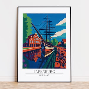 以下が含まれることがあります： ドイツ、パーペンブルクのカラフルなイラストが描かれた、額入りのアートプリント。赤いレンガ造りの建物の近くに停泊している大型船が描かれており、手前には自転車と運河があります。空は青く、白い雲が浮かんでいます。