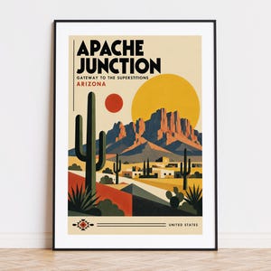 May include: A framed travel poster featuring the text Apache Junction Gateway to the Superstitions Arizona United States. The illustration depicts a desert landscape with a large saguaro cactus, a red sun, mountains, and small buildings.
