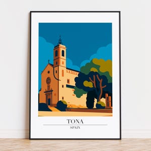 May include: A framed art print featuring a stylized illustration of a church in Tona, Spain. The artwork uses a limited color palette of beige, blue, and green. The text "TONA SPAIN" is printed at the bottom of the image.