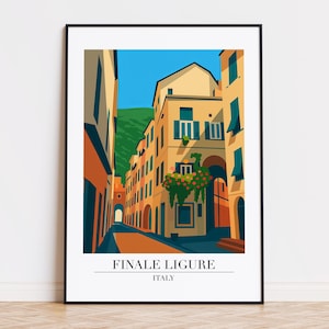 May include: A framed art print showing a stylized illustration of Finale Ligure, Italy. The artwork depicts a narrow street with buildings in yellow, orange, and blue, with a mountain in the background. The text "FINALE LIGURE ITALY" is at the bottom.