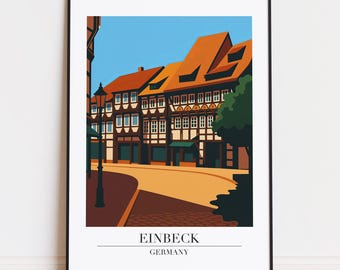 Könnte beinhalten: Ein gerahmter Kunstdruck mit einer stilisierten Illustration von Einbeck, Deutschland. Das Kunstwerk zeigt traditionelle Fachwerkhäuser mit orangefarbenen Dächern und blauem Himmel. Der Druck enthält den Text "EINBECK GERMANY" am unteren Rand.