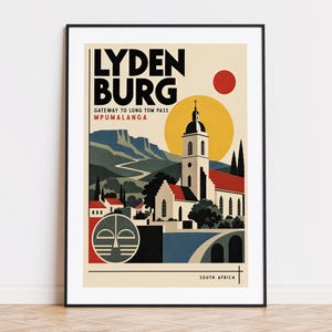 Op de afbeelding: Een ingelijste reisposter met de tekst LYDEN BURG GATEWAY TO LONG TOM PASS MPUMALANGA SOUTH AFRICA. De illustratie toont een kerk met een rood dak, een grote gele zon, een rode cirkel, bergen en een rond embleem in crème, blauw, rood en zwart.