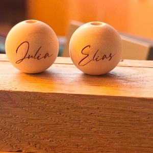 Op de afbeelding: Twee houten kralen met de namen "Julia" en "Elias" erop gegraveerd.