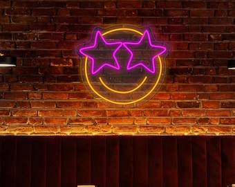 May include: A neon sign with a yellow smiley face and two pink star-shaped eyes. The sign is hanging on a brick wall above a red velvet booth with two tables and chairs.