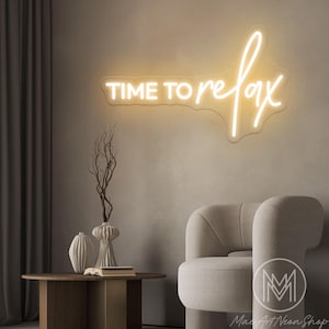 Puede incluir: Un letrero de neón con las palabras "TIME TO relax" en una escritura fluida, que emite un brillo cálido y acogedor. El letrero está montado en una pared de tonos neutros, encima de una pequeña mesa con jarrones decorativos y un sillón moderno. La estética general es minimalista y relajante.