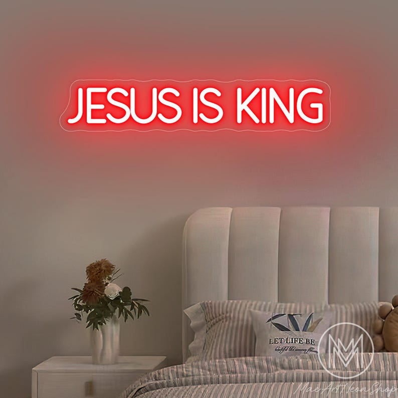 K&ouml;nnte beinhalten: Ein rotes Neonzeichen mit der Aufschrift &bdquo;JESUS IS KING&ldquo; ist &uuml;ber einem Bett an der Wand angebracht. Der Raum ist mit einem Nachttisch, Blumen und Kissen dekoriert. Das Schild erhellt den Raum mit einem warmen Schein.