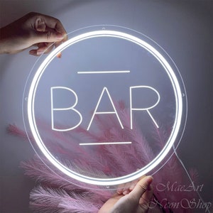 Op de afbeelding: Wit neon-bord in een ronde vorm met het woord "BAR" in het midden. Het bord is verlicht en heeft een witte rand.