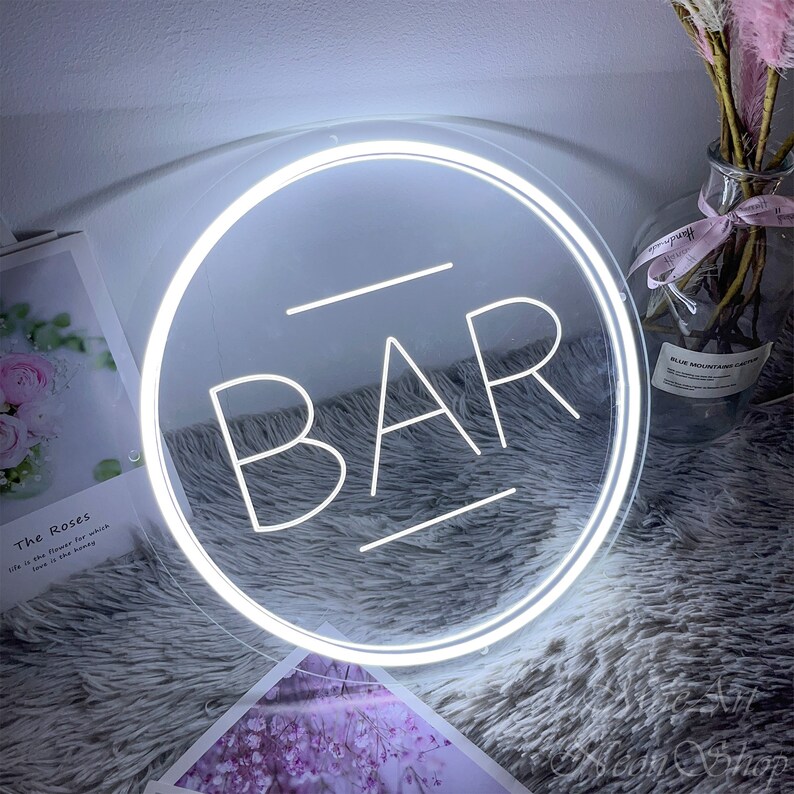 Op de afbeelding: Wit neon-bord met een ronde lijst en het woord "BAR" in witte neon-letters.