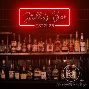 May include: A red neon sign displaying "Stella's Bar" and "EST 2026". Below the sign is a bar shelf stocked with bottles of spirits. The bar has a classic, vintage style.