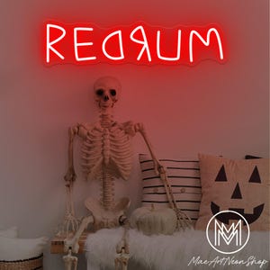 Puede incluir: Un letrero de neón rojo que dice "REDRUM" está montado sobre un esqueleto sentado en un banco con almohadas y una calabaza. La escena está decorada para Halloween. El letrero es un elemento visual llamativo.