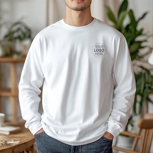 May include: A white long-sleeve shirt with a crew neck. The shirt features a circular logo design on the upper left chest that reads "YOUR LOGO HERE" in black text. The shirt is made of a soft, opaque material.