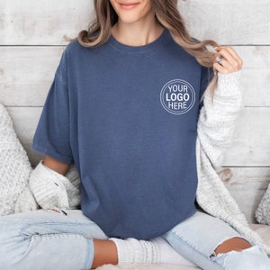 May include: A blue t-shirt with a white circle on the front that says "YOUR LOGO HERE".