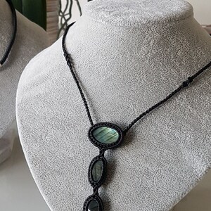 Puede incluir: Un collar de cord&oacute;n negro con tres piedras de labradorita de forma ovalada. Las piedras son de color verde oscuro y azul con un brillo iridiscente.