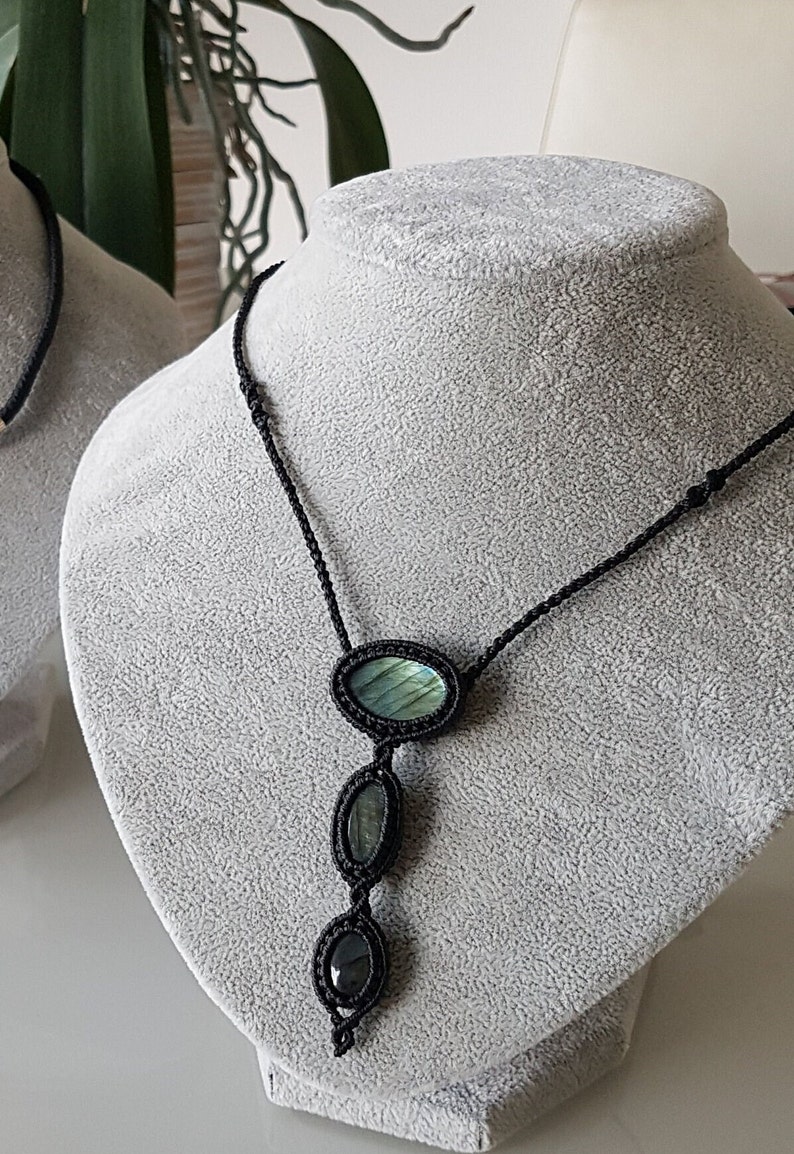 Puede incluir: Un collar de cord&oacute;n negro con tres piedras de labradorita de forma ovalada. Las piedras son de color verde oscuro y azul con un brillo iridiscente.