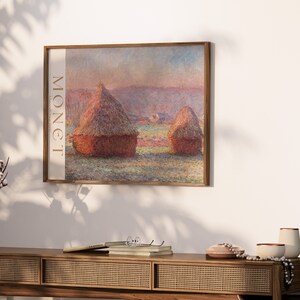 May include: A framed print of a Monet painting depicting two haystacks in a field, with the word "MONET" printed vertically on the left. The artwork is displayed above a wooden console table with decorative items.
