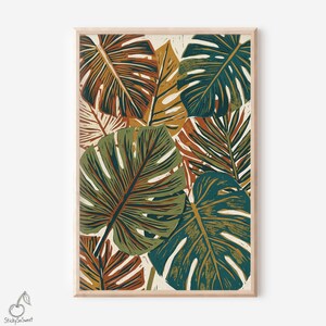 May include: A framed botanical print featuring a collage of stylized tropical leaves in shades of green, brown, and gold. The leaves have a textured, block-print appearance, creating a layered and artistic composition. The print is set against a cream-colored background.