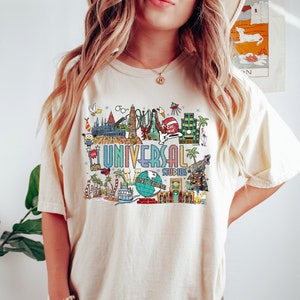 May include: A white t-shirt with a colorful graphic of Universal Studios attractions, including the Hogwarts castle, the Jurassic Park ride, and the Simpsons ride. The text "Universal Studios" is printed in a colorful font.