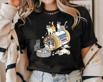 May include: A black t-shirt with a graphic of a pill bottle filled with cartoon cats. The text on the bottle reads "Serotonin Booster" and "Side Effects: Cute Aggression".