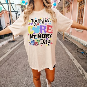 May include: A light beige t-shirt with the text "Today is a CORE MEMORY Day" in colorful letters. The shirt features a Mickey Mouse head with a rainbow inside and a group of characters from the movie Inside Out.
