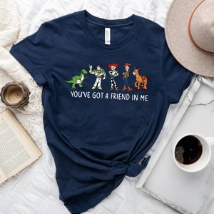 May include: A navy blue t-shirt with a graphic of the Toy Story characters Woody, Buzz Lightyear, Rex, and a horse. The text "You've got a friend in me" is printed below the graphic.
