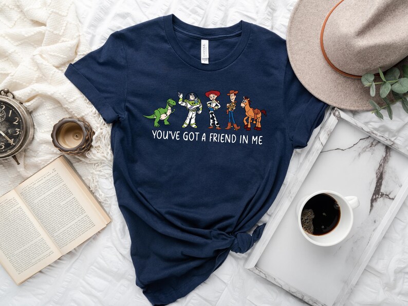 May include: A navy blue t-shirt with a graphic of the Toy Story characters Woody, Buzz Lightyear, Rex, and a horse. The text "You've got a friend in me" is printed below the graphic.