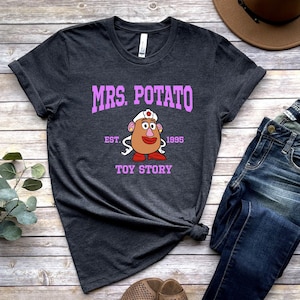 May include: A dark gray t-shirt with a pink graphic of Mrs. Potato Head from Toy Story. The graphic includes the text "Mrs. Potato", "Est. 1995", and "Toy Story".