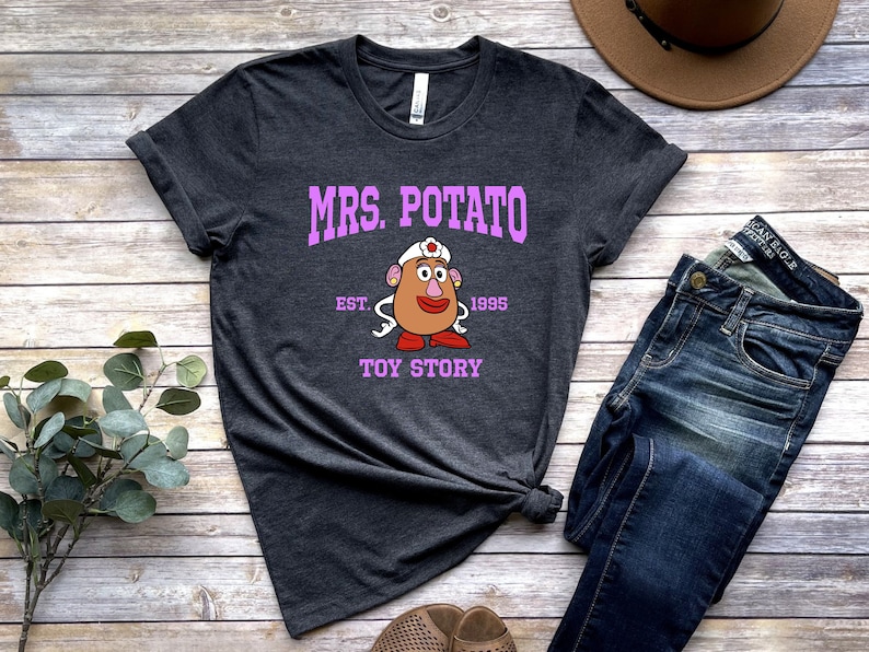 May include: A dark gray t-shirt with a pink graphic of Mrs. Potato Head from Toy Story. The graphic includes the text "Mrs. Potato", "Est. 1995", and "Toy Story".