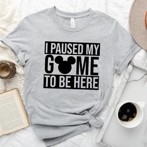 May include: Gray t-shirt with black text that reads "I paused my game to be here" with a black Mickey Mouse head replacing the "a" in "game".