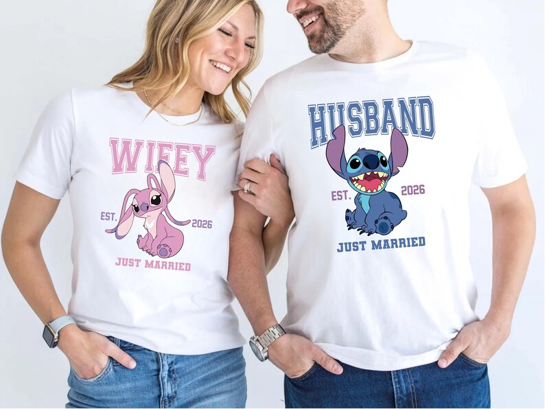 May include: White t-shirts with matching graphics. One shirt says "Wifey" with a pink cartoon character and the other says "Husband" with a blue cartoon character. Both shirts have "EST. 2026" and "JUST MARRIED".