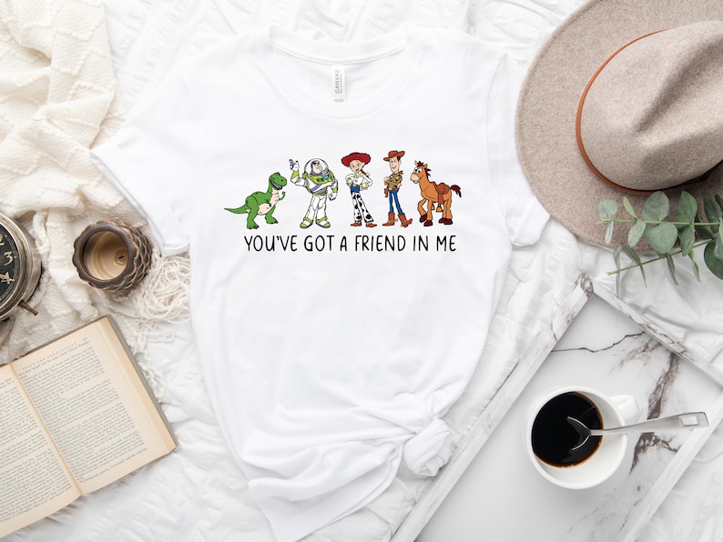 May include: White t-shirt with a graphic of characters from the Toy Story movie franchise. The characters are lined up in a row and include Rex, Buzz Lightyear, Jessie, Woody, and Bullseye. The text "You've got a friend in me" is printed below the characters.
